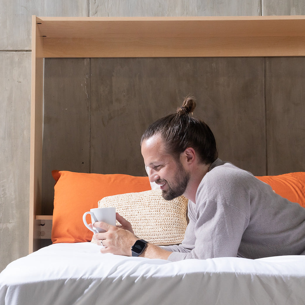 Smiling man laying on a murphy bed while drinking coffe